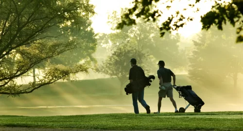 Golfers walking on the course in sunlight and fog